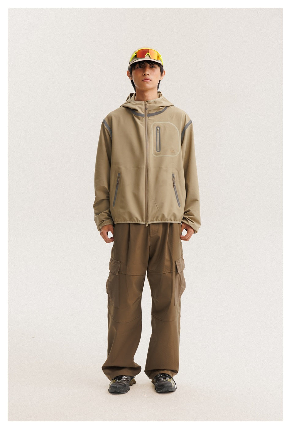 Front view of a model wearing a tan hooded zip jacket with gray trim and brown cargo pants.