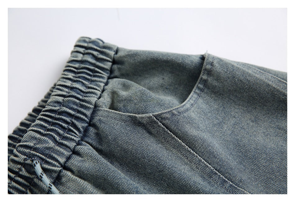 Close-up of a curved pocket opening beside the gathered elastic waistband on faded blue denim pants.
