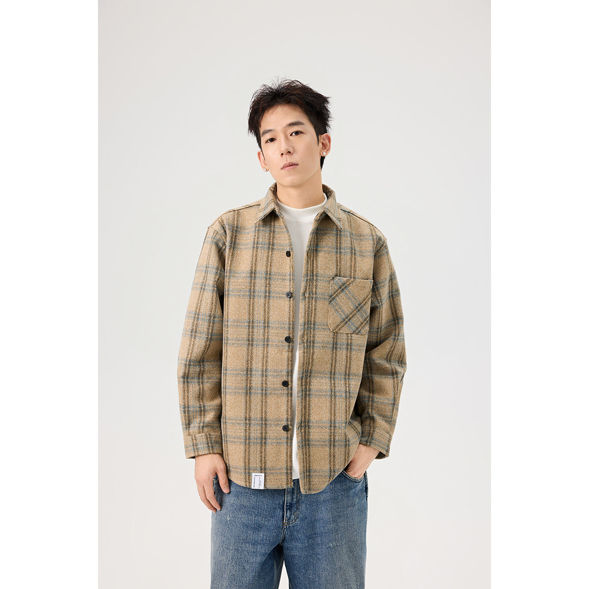 Closer view of a man wearing a tan and blue plaid button-front overshirt over a white shirt.