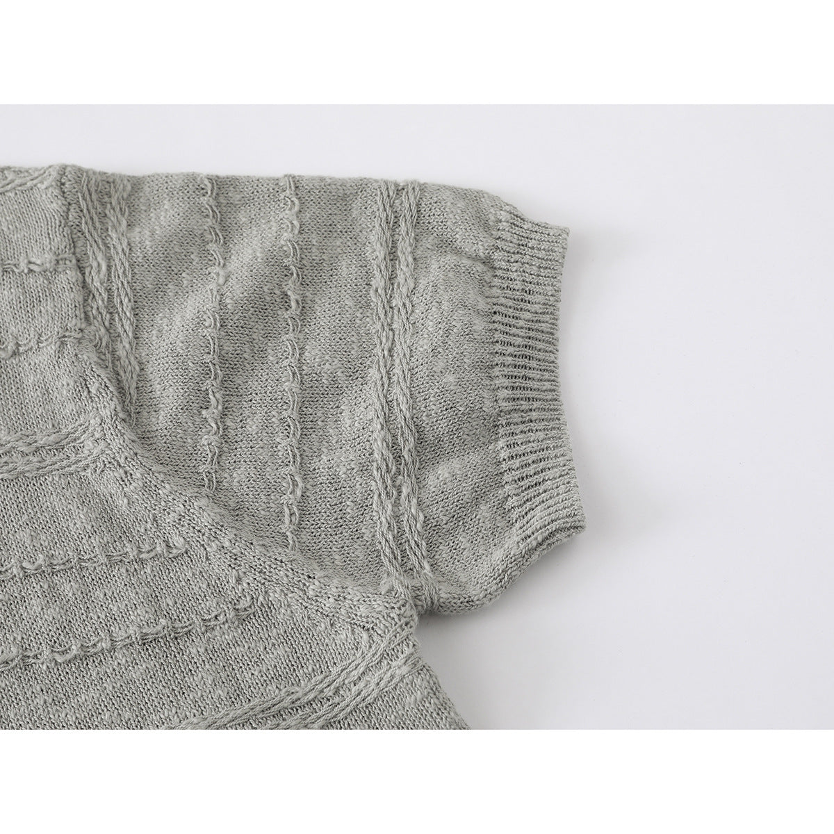 Close-up of a light gray knit polo shirt sleeve with ribbed cuff and textured bands.