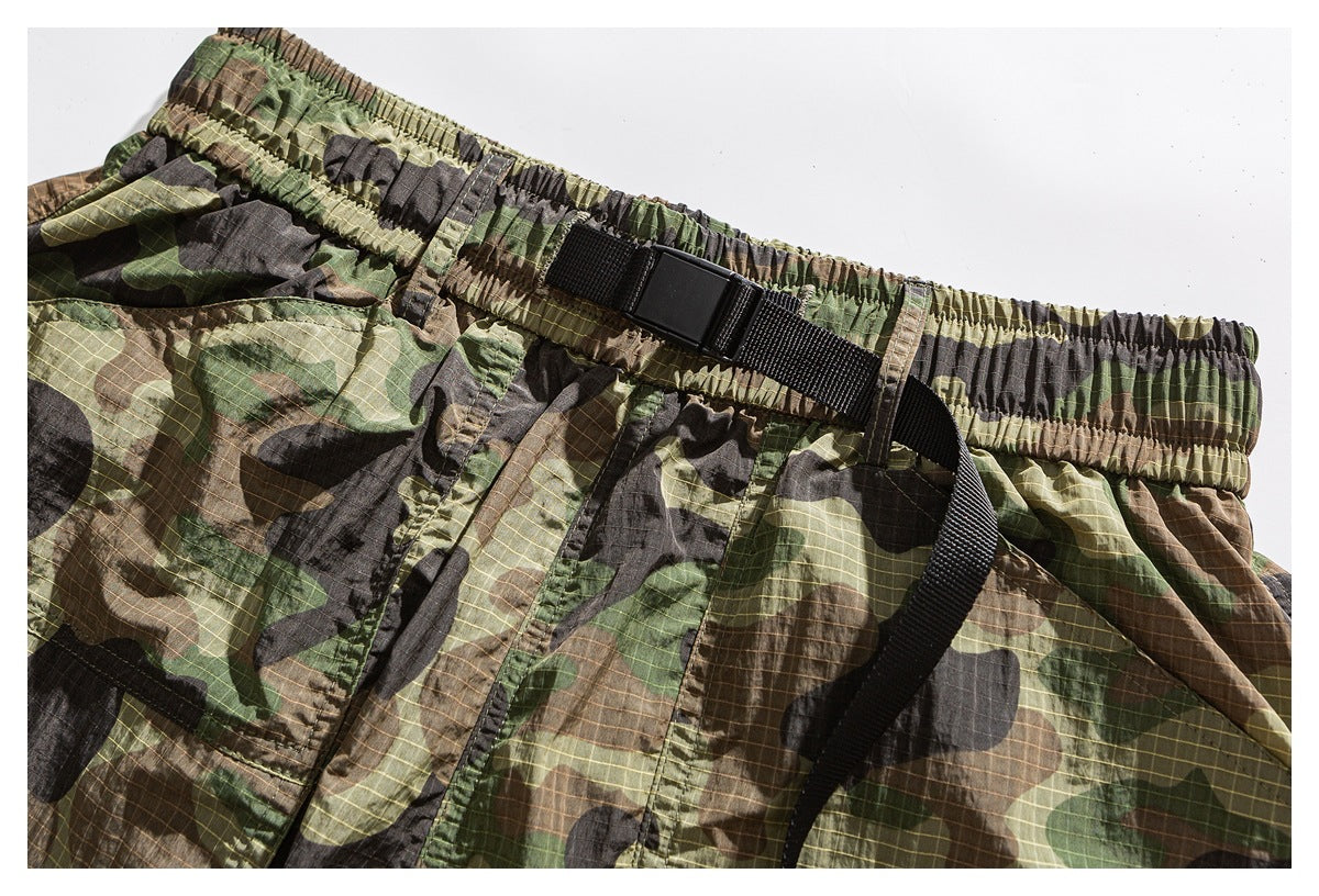Close-up of camouflage shorts showing the elastic waistband, black adjustable belt and front stitching.