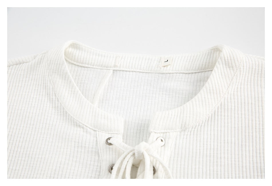 Close-up of an off-white ribbed top showing its rounded neckline and lace-up front with metal eyelets.