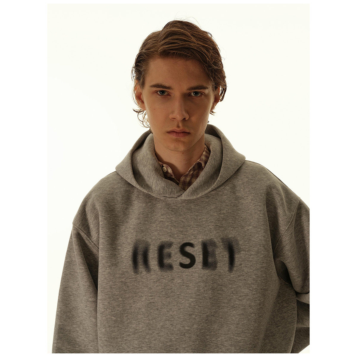 Close view of a model wearing a heather-gray hoodie with dark blurred lettering across the chest.