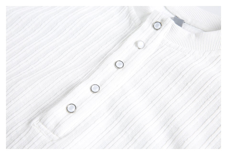 Close-up of a white ribbed shirt's snap-button placket and textured fabric.