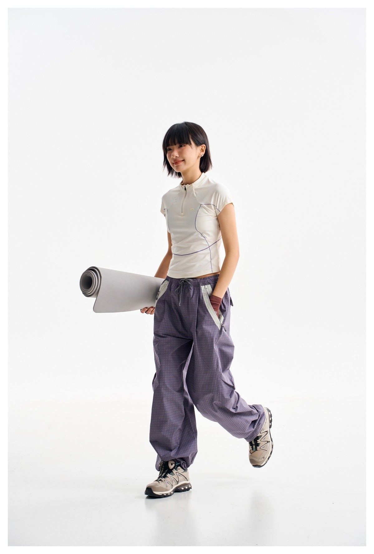 A woman models a white short-sleeve zip-neck top with curved purple seams and loose purple plaid pants.