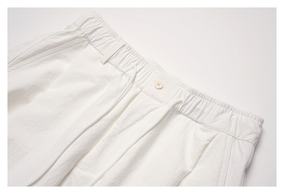 Close-up of off-white trousers showing the gathered waistband, button closure, belt loops and drawcord.