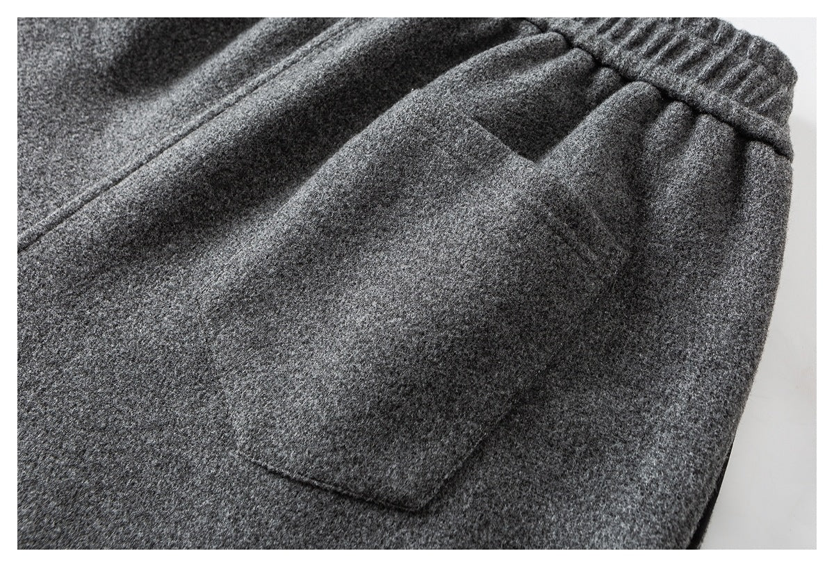 Close-up of charcoal gray trousers showing a large patch pocket below the gathered waistband.