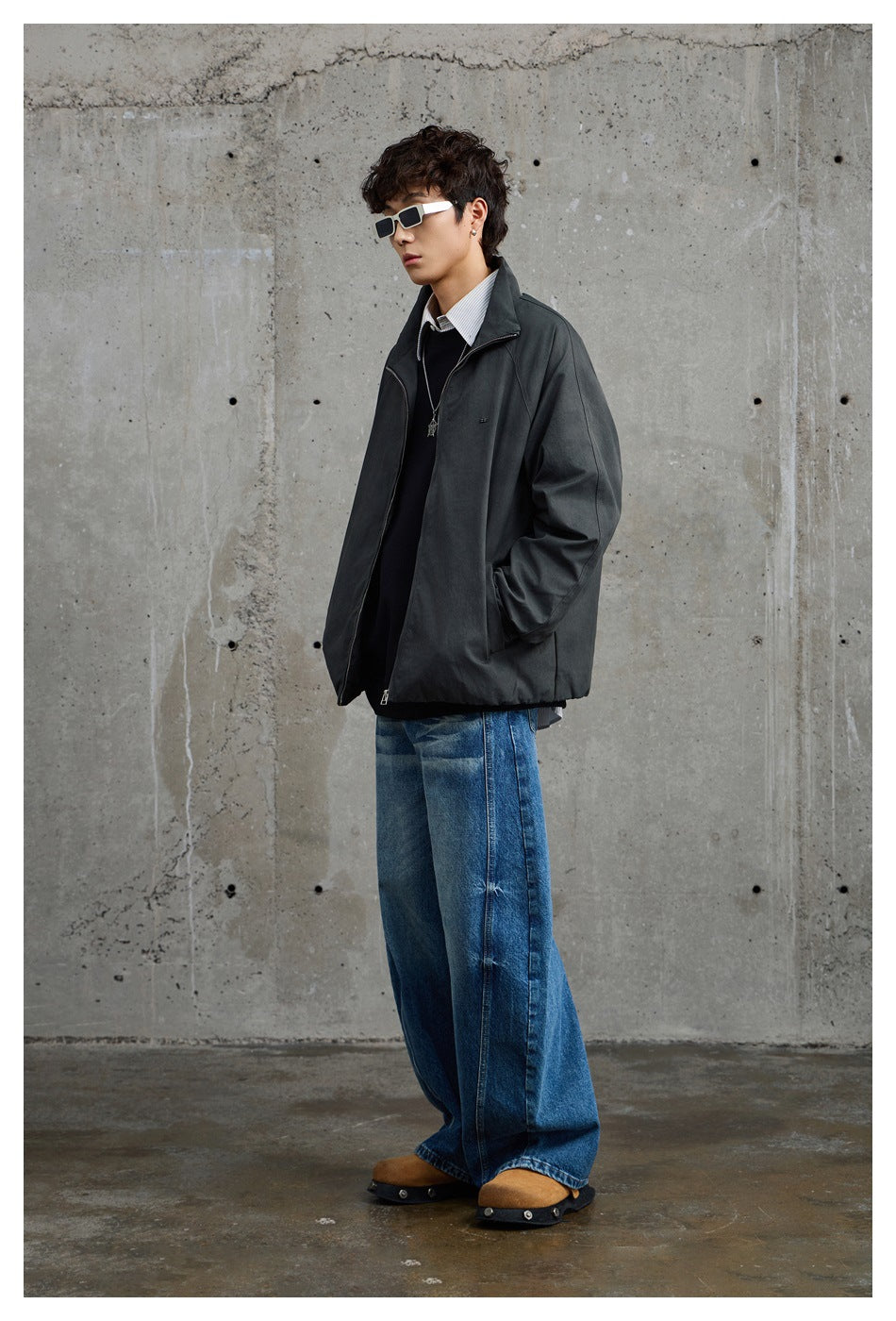Side view of a model wearing a charcoal-gray jacket with wide blue jeans and sunglasses.
