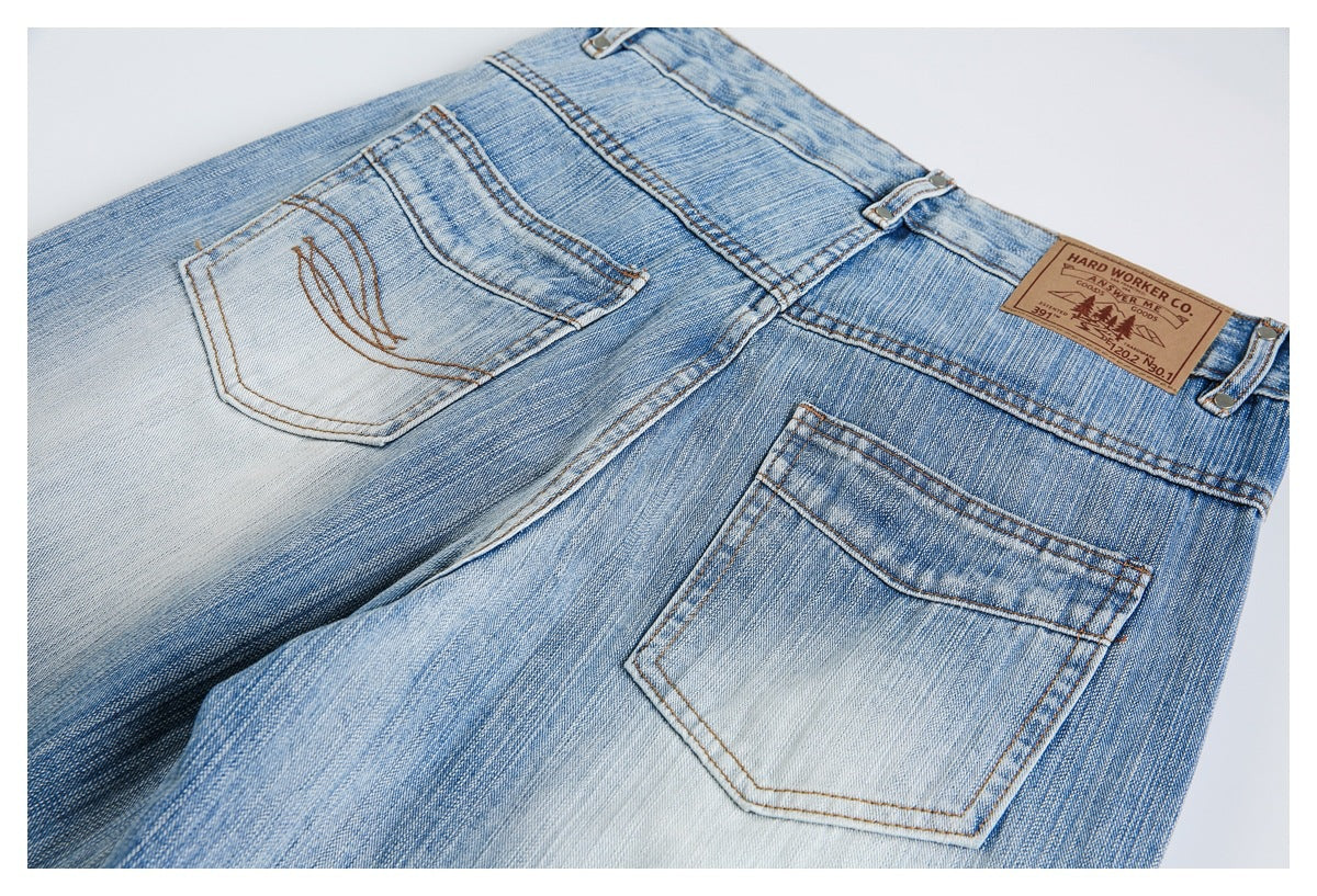 Close-up of the back of light blue jeans, showing two stitched pockets, belt loops and a leather waistband patch.