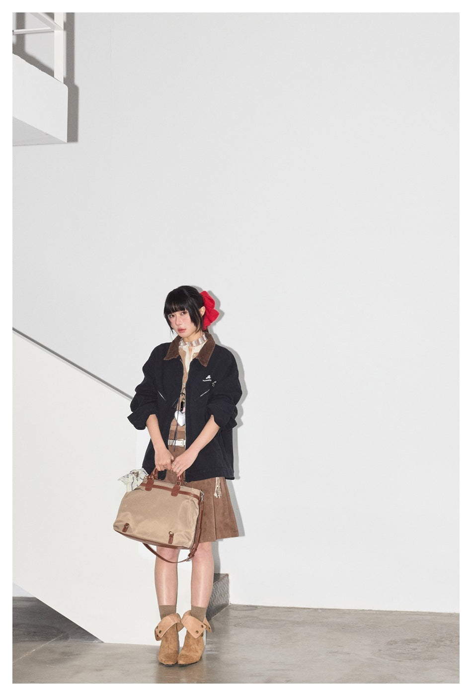 Full-length model wearing a dark navy jacket with a brown collar and a brown skirt, holding a tan handbag.