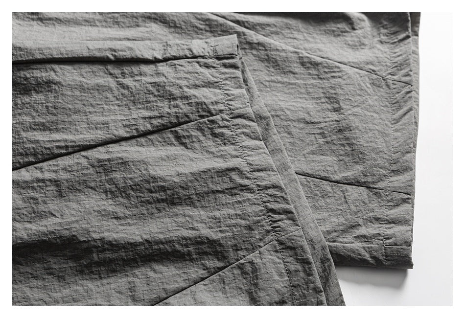 Close-up of gray cargo pants showing a large flap pocket, panel seams, and crinkled surface texture.