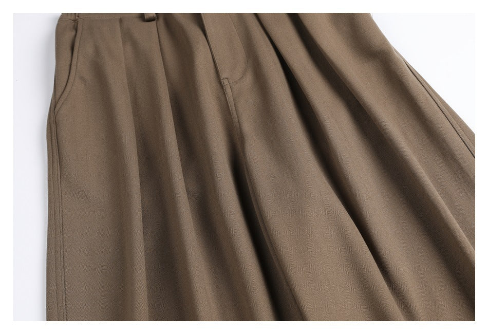 Close-up of taupe-brown trousers showing a side pocket, pleats, and fabric texture.