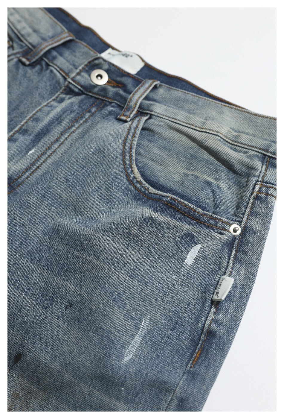 Close-up of faded blue jeans showing the front pocket, metal button, belt loop and distressed marks.