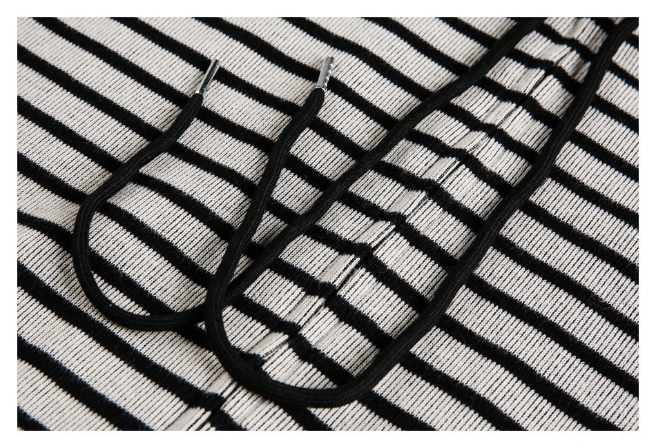 Close-up of black drawstrings with metal tips over black-and-white striped knit fabric.