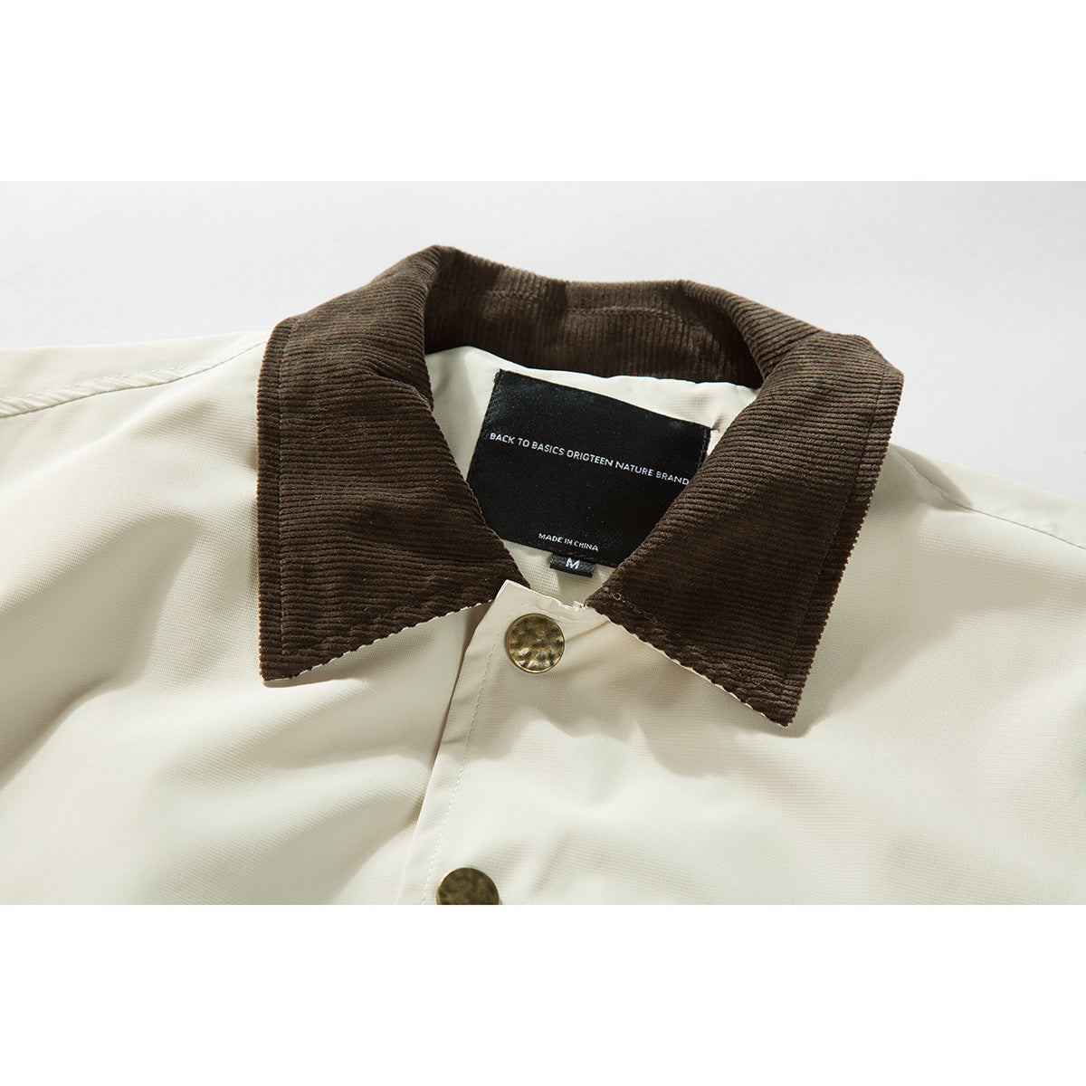 Close-up of an ivory jacket with a dark brown corduroy collar, brass-tone buttons, and a visible neck label.
