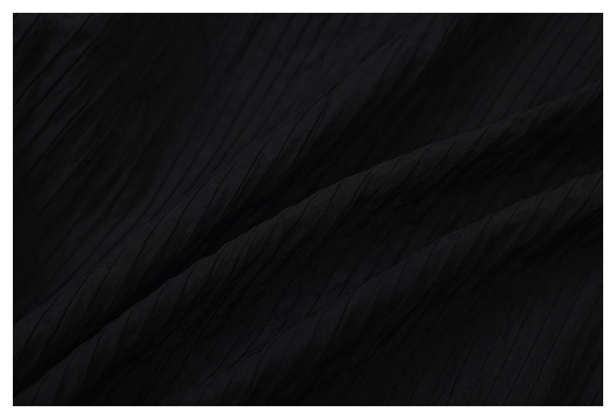Close-up of black fabric showing fine vertical ribbed pleats and soft folds.