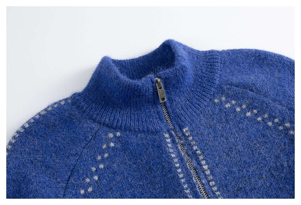 Close-up of a blue knit sweater with a high ribbed collar, metal zipper, and small light-colored motifs.