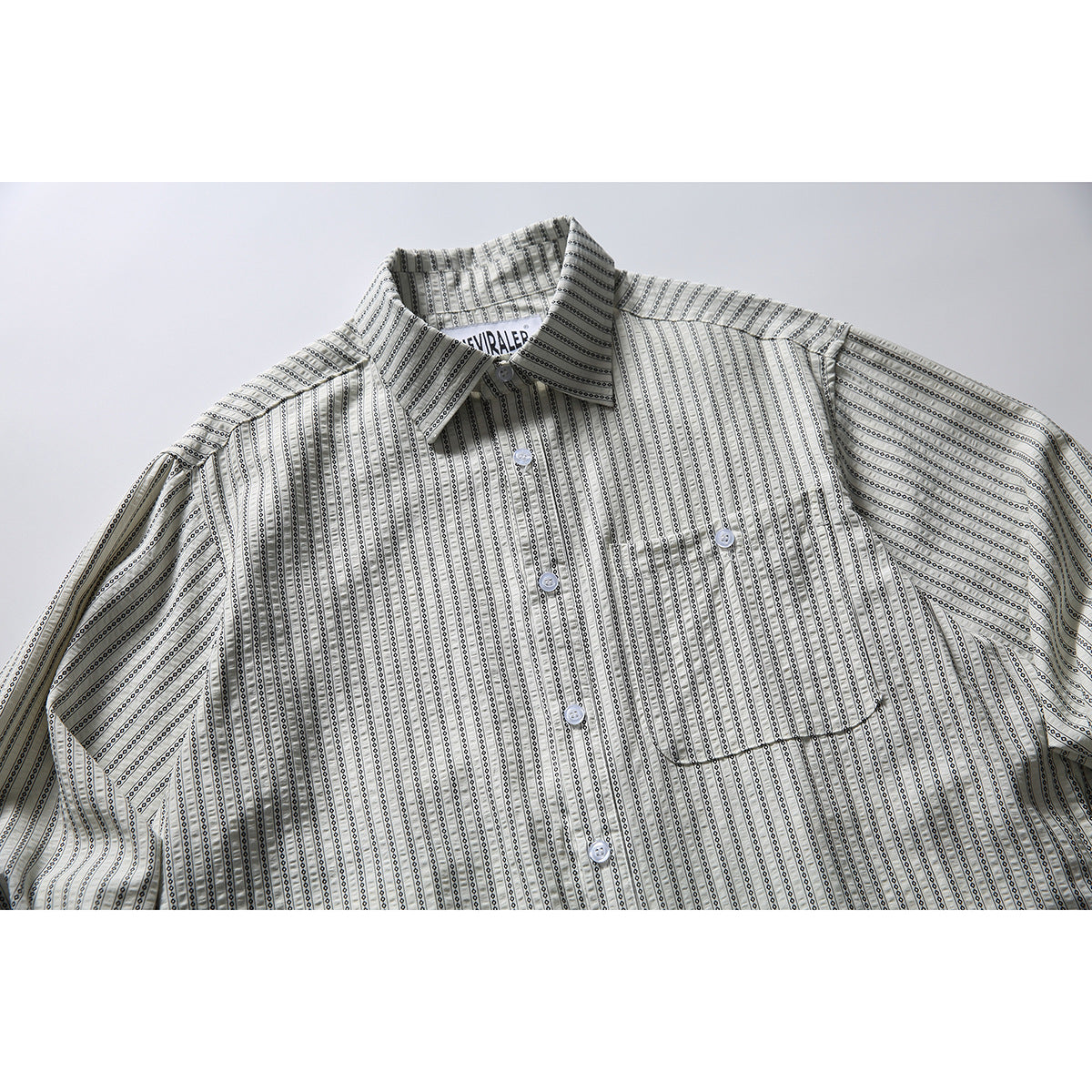 Close view of a light shirt with narrow black geometric stripes, a pointed collar, buttons, and a chest pocket.