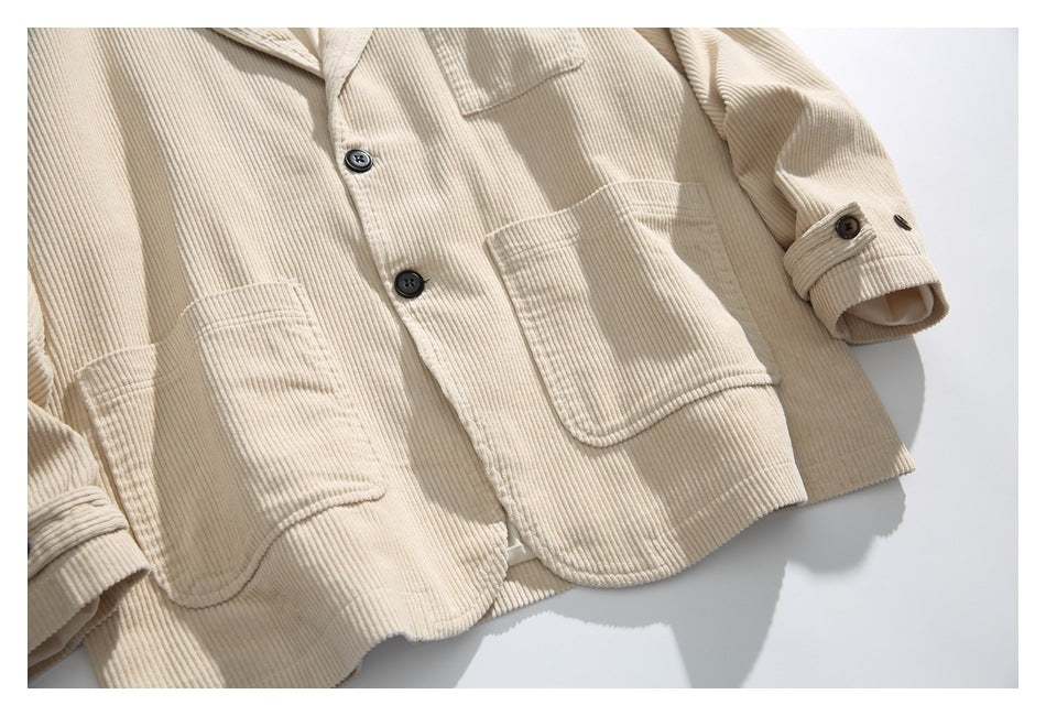 Close-up of the cream corduroy jacket front with patch pockets, dark buttons and buttoned cuffs.