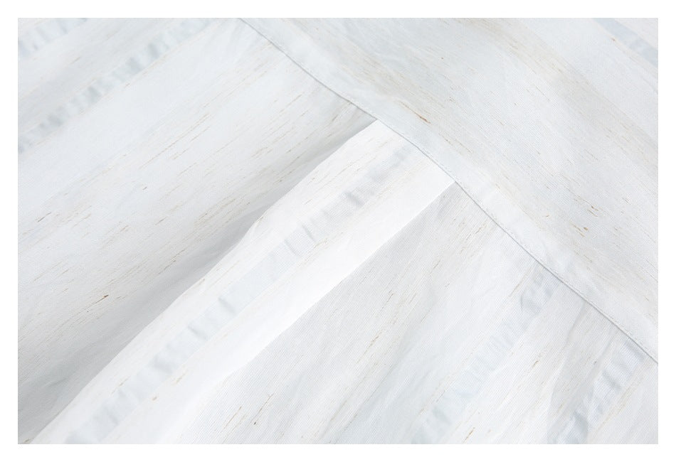 Close-up of overlapping white shirt panels and stitched seams, with subtle tan streaks and pale blue accents.