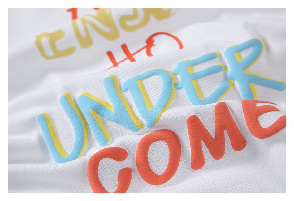 Close-up of colorful raised lettering on white T-shirt fabric, including blue, yellow, and coral text.