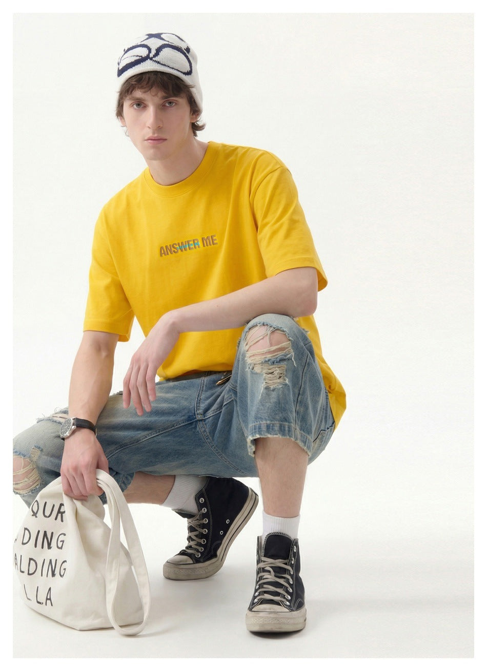 Seated model wearing a yellow T-shirt with chest lettering, shown from the front.