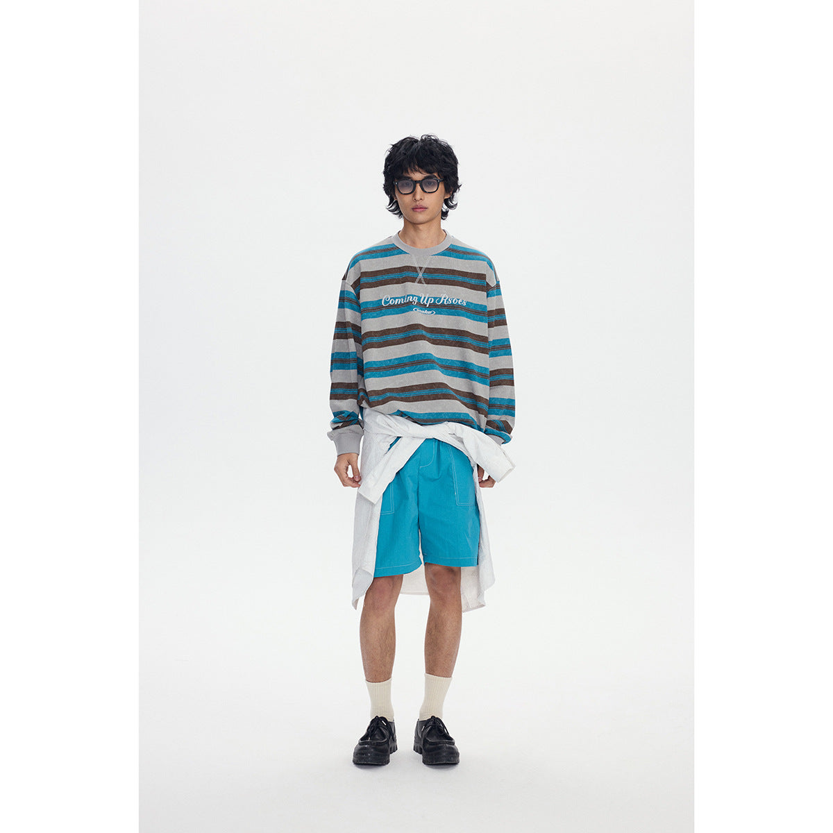 Front view of a model wearing a gray, teal, and brown striped sweatshirt with bright teal shorts and a white shirt tied at