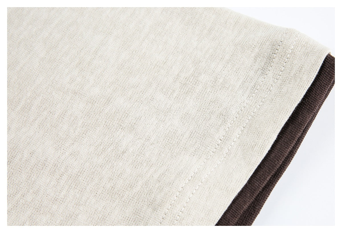 Close-up of a cream short sleeve with a stitched hem and dark brown contrast fabric beneath.