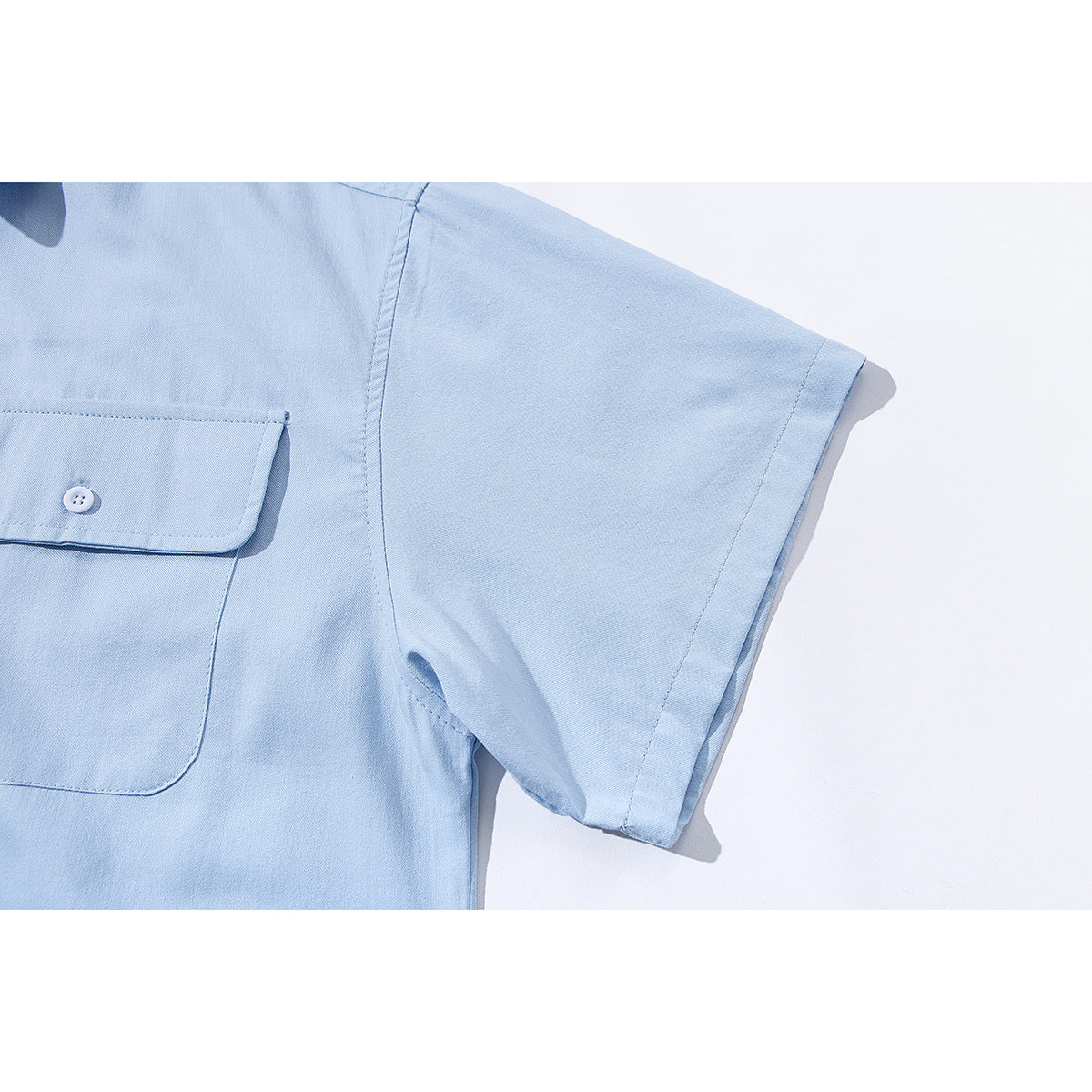 Close-up of a light blue short-sleeve shirt showing the sleeve seam and flap pocket.