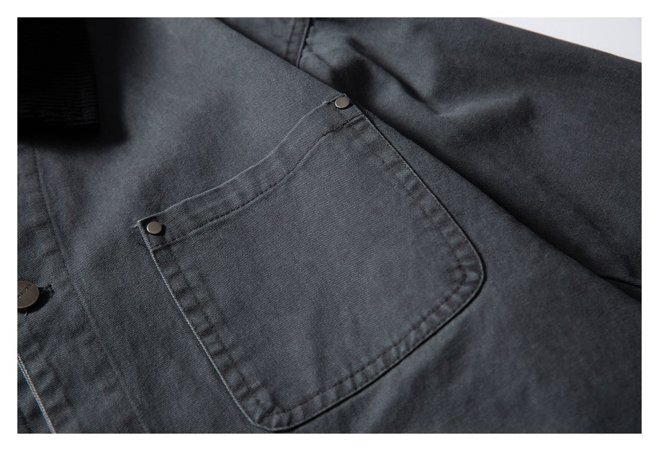 Close-up of a charcoal jacket's large front pocket, showing its stitching and two small metal rivets.