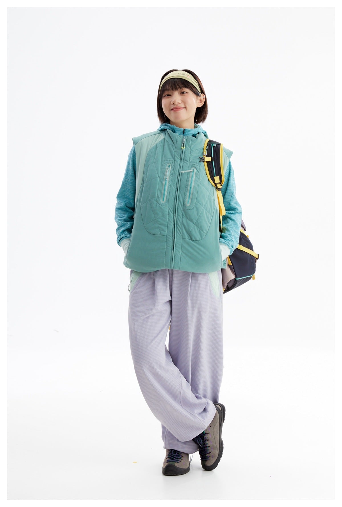 Model in a teal quilted sleeveless vest over a blue hooded top, paired with loose lavender pants.