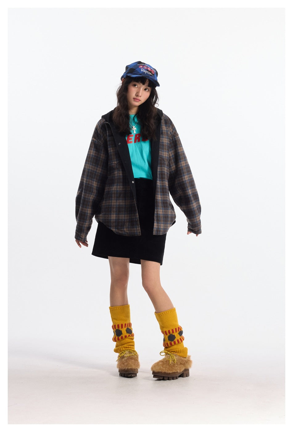 Model wearing oversized plaid hooded jacket open over a teal tee and black skirt