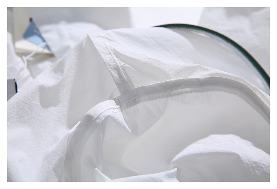Close-up of a white garment's curved stitched edge and interior seam, with dark green trim in the background.