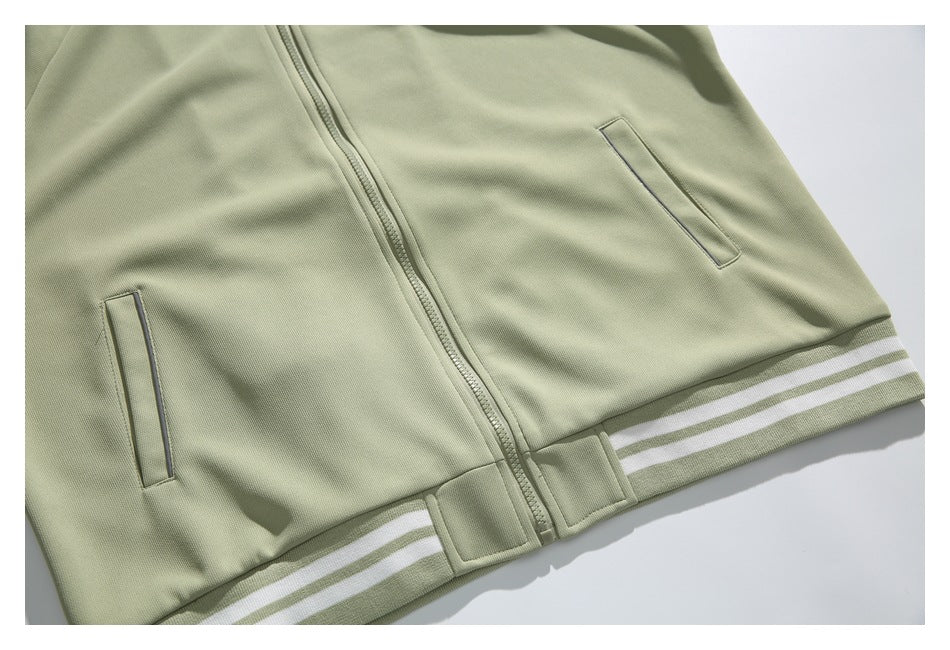 Close-up of a pale sage zip-front jacket with angled pockets and a striped ribbed hem, laid flat.