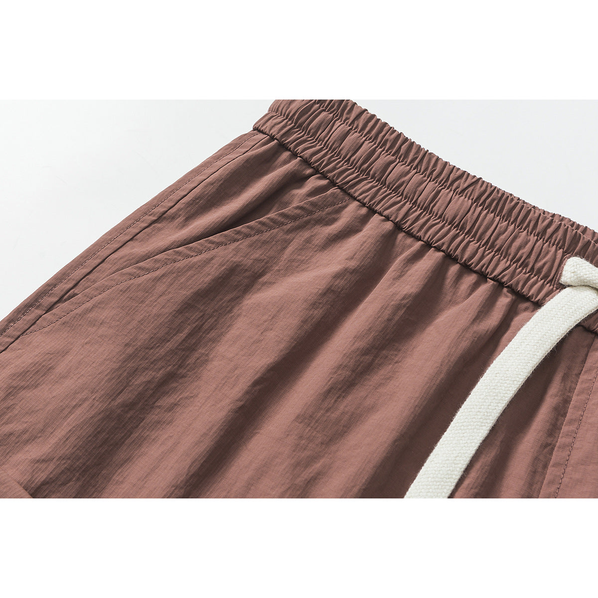 Close-up of dusty mauve shorts showing the gathered elastic waistband, white drawcord, and stitched fabric.