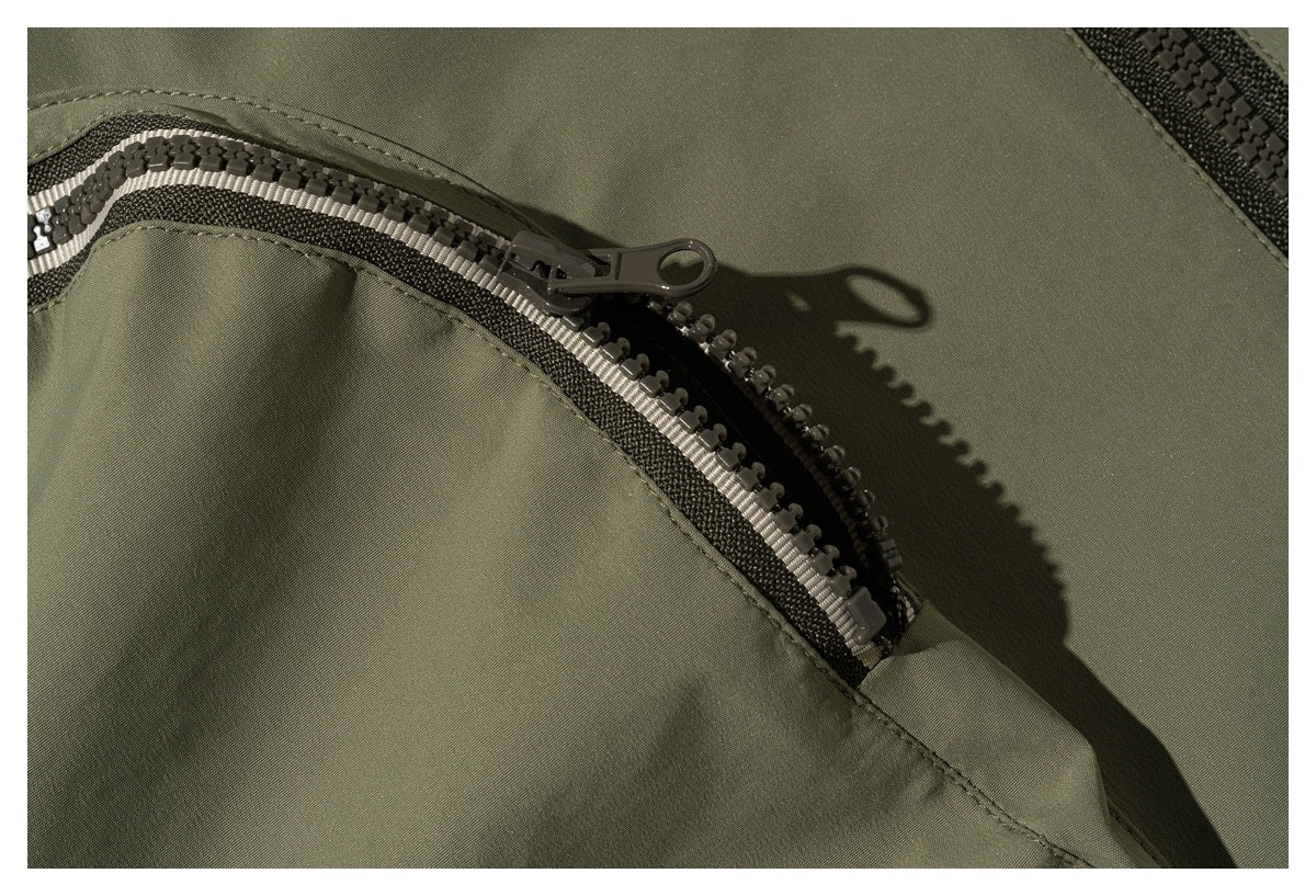 Close-up of a two-tone zipper and pull on an olive jacket pocket.