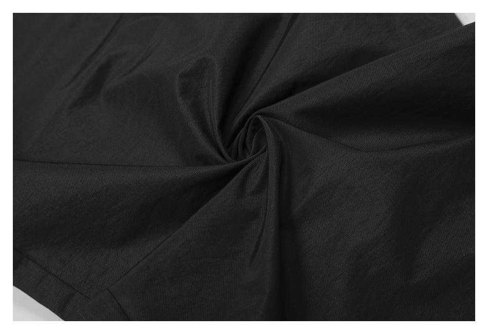 Close-up of black pant fabric gathered into folds to show its surface and drape.