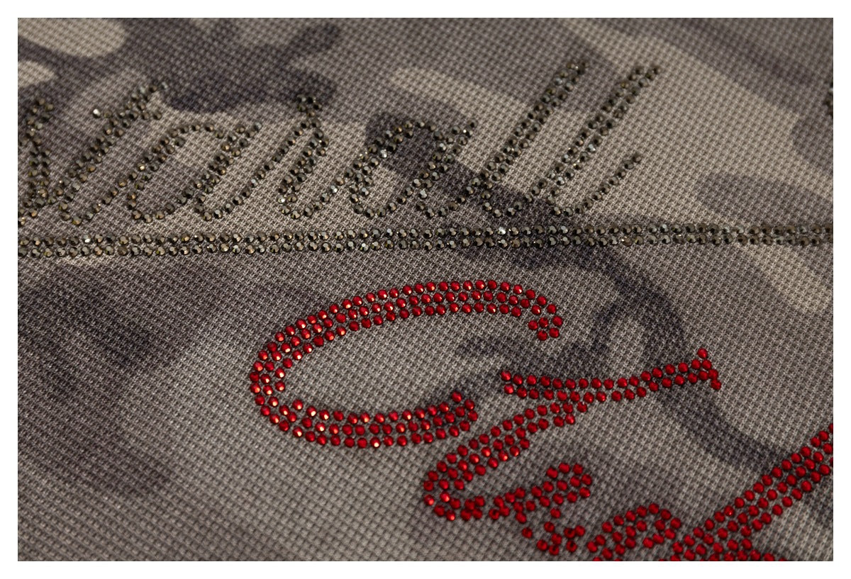Close-up of black and red rhinestone lettering on gray-brown camouflage fabric.