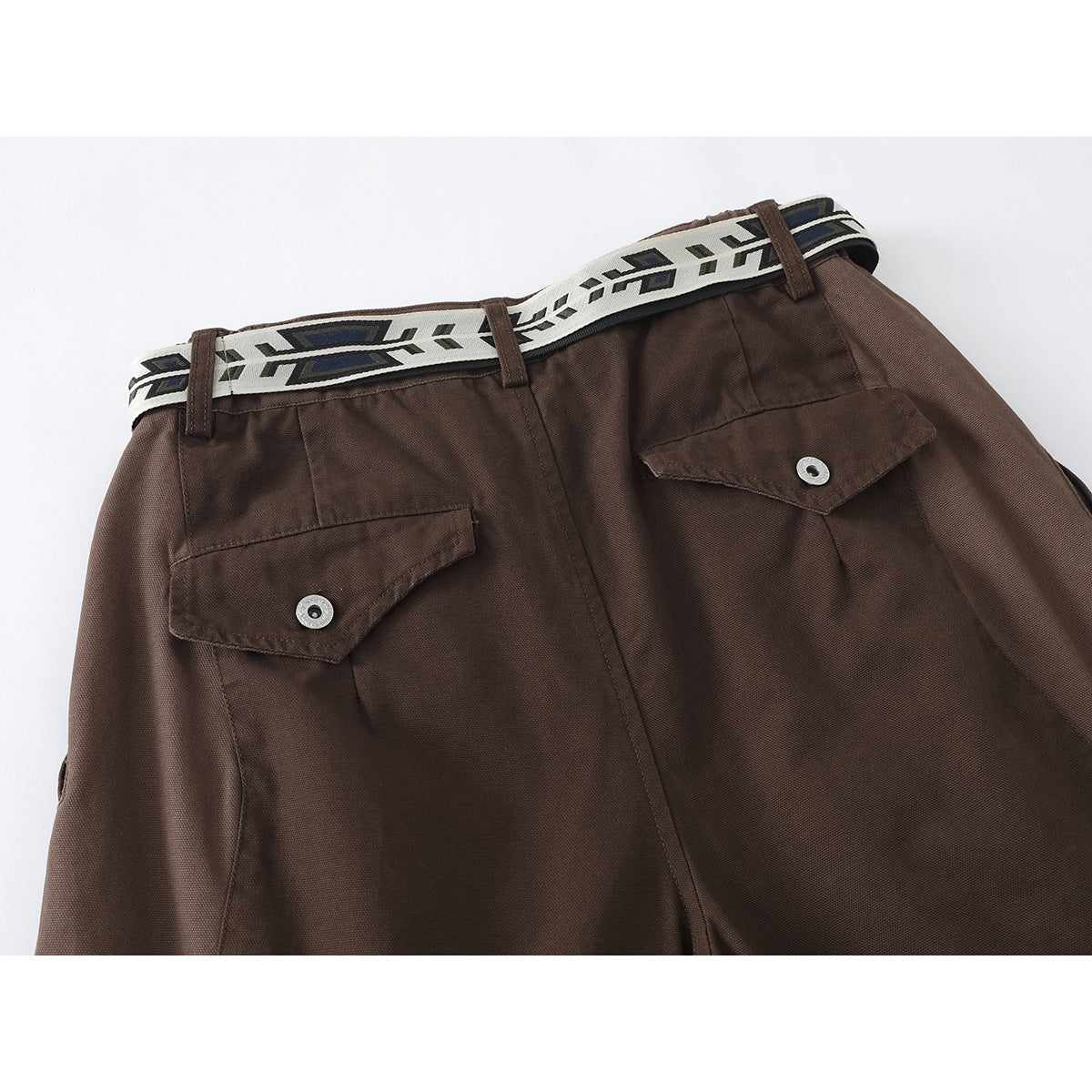 Close-up of brown trousers with two buttoned back flap pockets and a patterned cream belt.