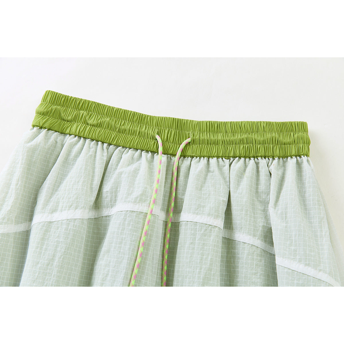 Close-up of a lime elastic waistband and neon drawcords on a pale green grid-patterned skirt.