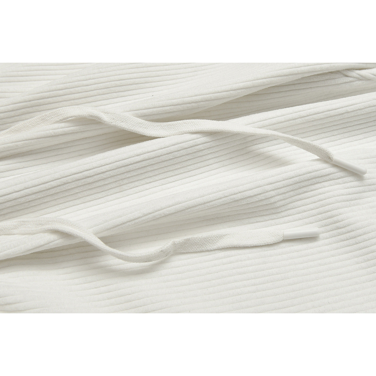 Close-up of two white drawstrings with plastic tips against the ribbed fabric of white pants.