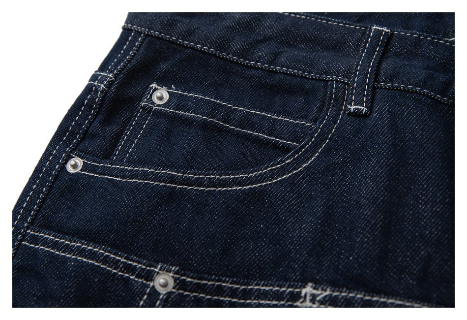 Close-up of dark indigo jeans showing a front pocket, coin pocket, belt loop, and contrast stitching.