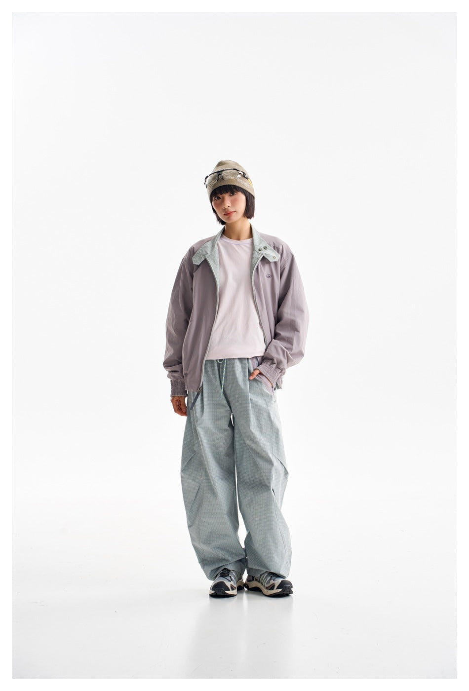 Model wearing a lavender-gray zip jacket with pale green collar panels and loose pale green checked trousers.