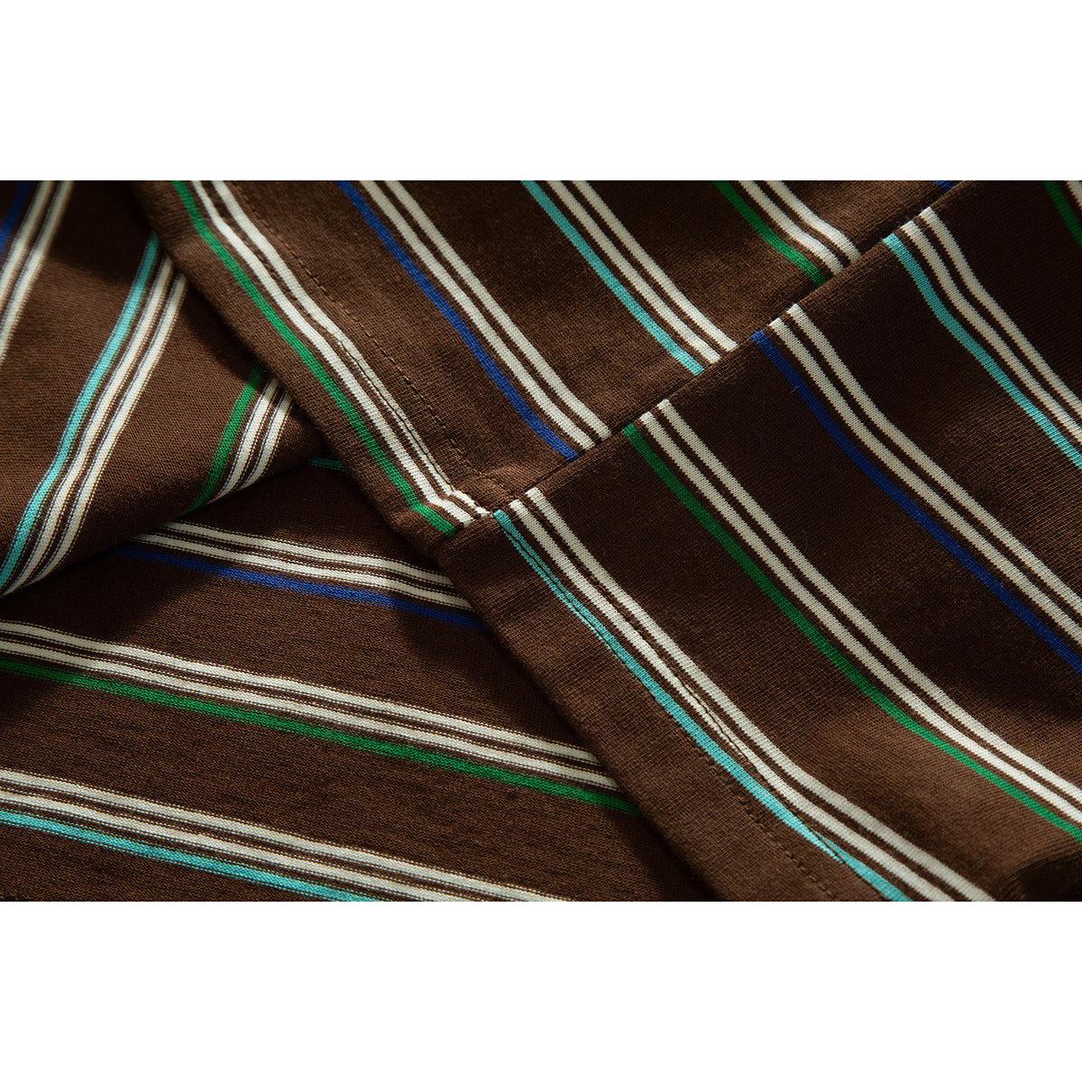 Close-up of brown striped shirt fabric and a stitched seam, with cream, green, turquoise, and blue stripes.