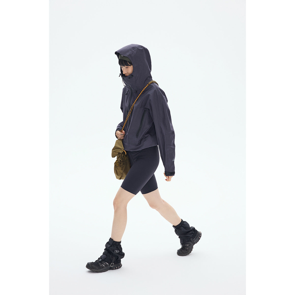A person walks wearing a dark charcoal hooded jacket, black shorts, and hiking gear.