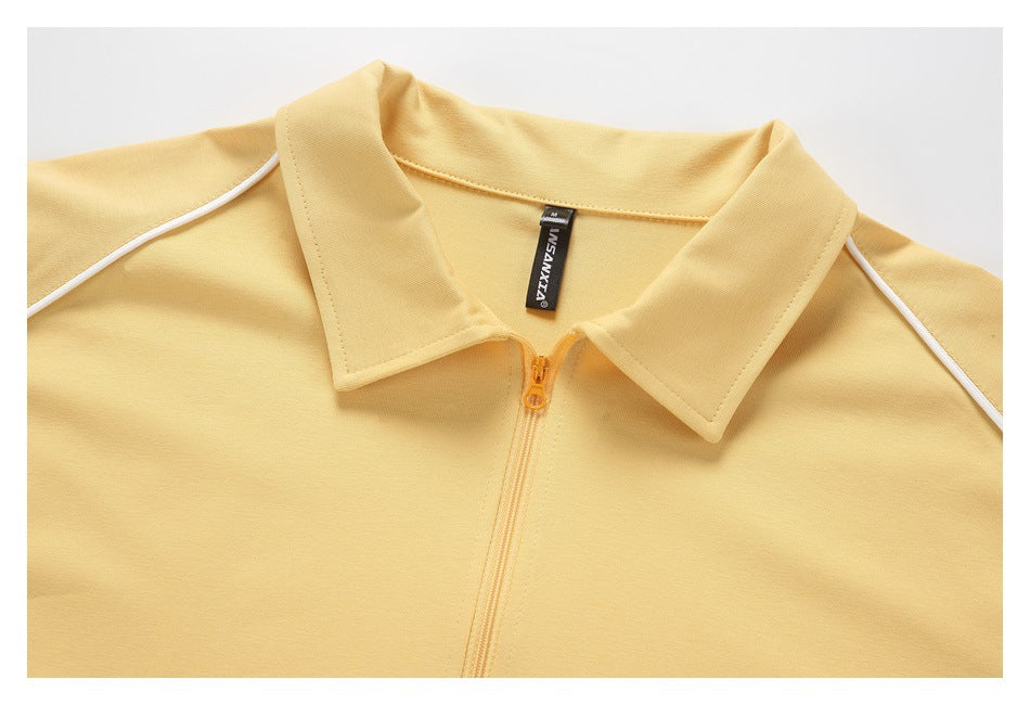 Close-up of a pale yellow collared top with a short zipper, white shoulder piping and a black neck label.