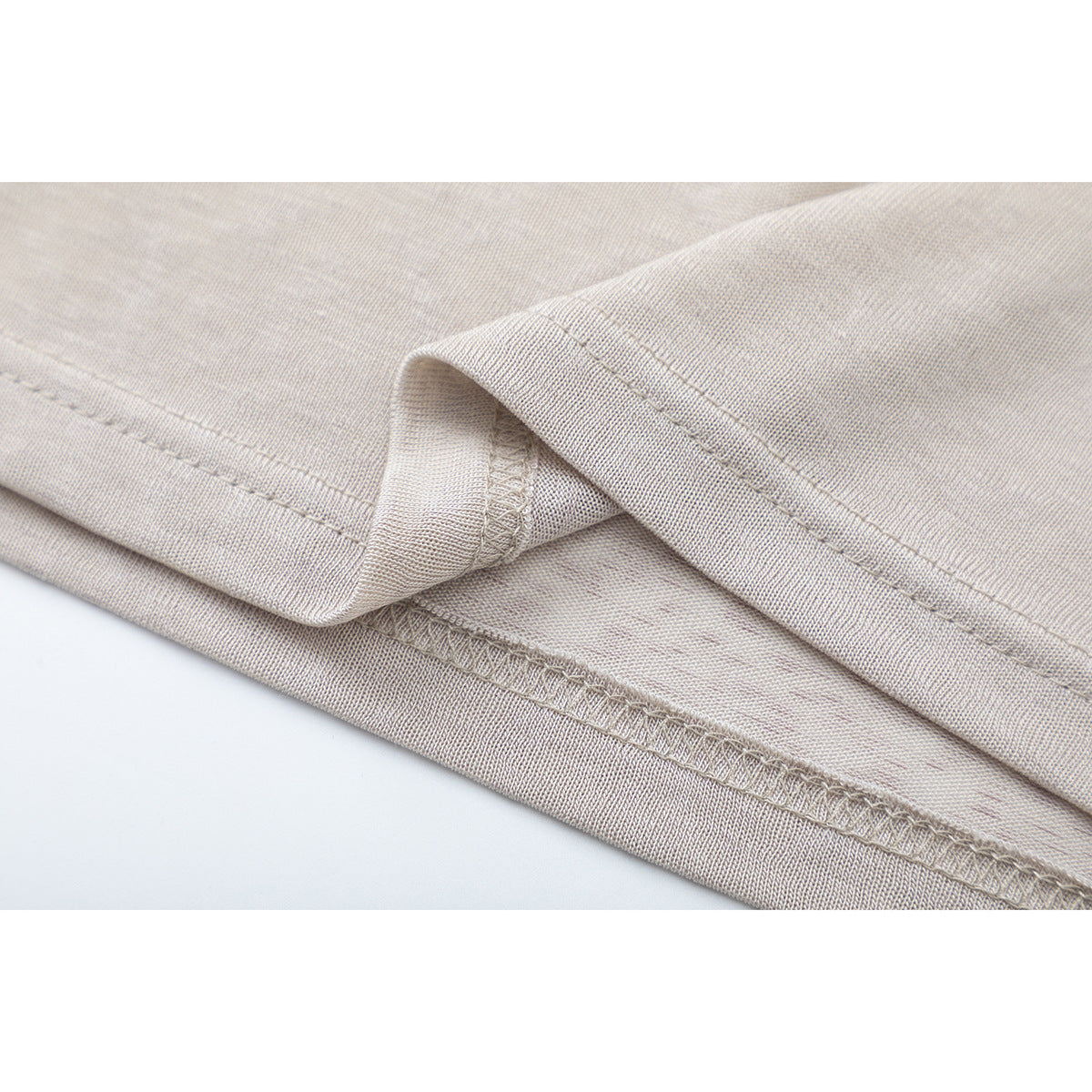 Close-up of the light beige shirt's folded hem and parallel stitching.