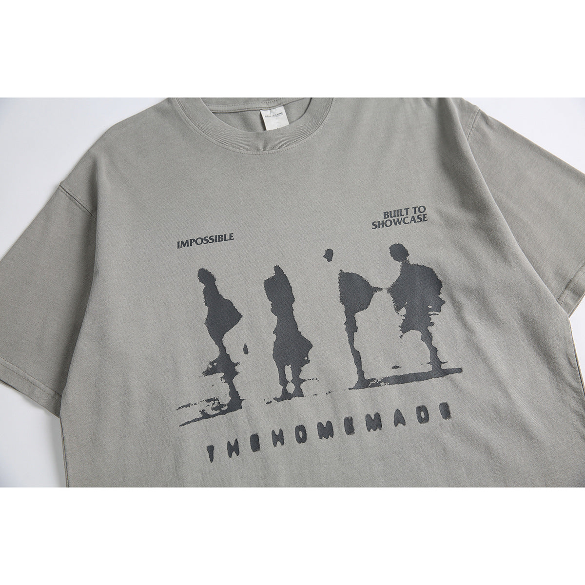 Close-up of a gray T-shirt front with a dark graphic of silhouetted figures and English lettering.
