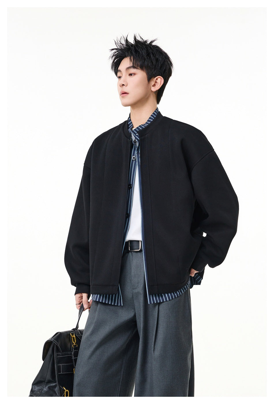 Model wearing a black oversized jacket over a blue striped shirt, shown from the front with gray trousers.
