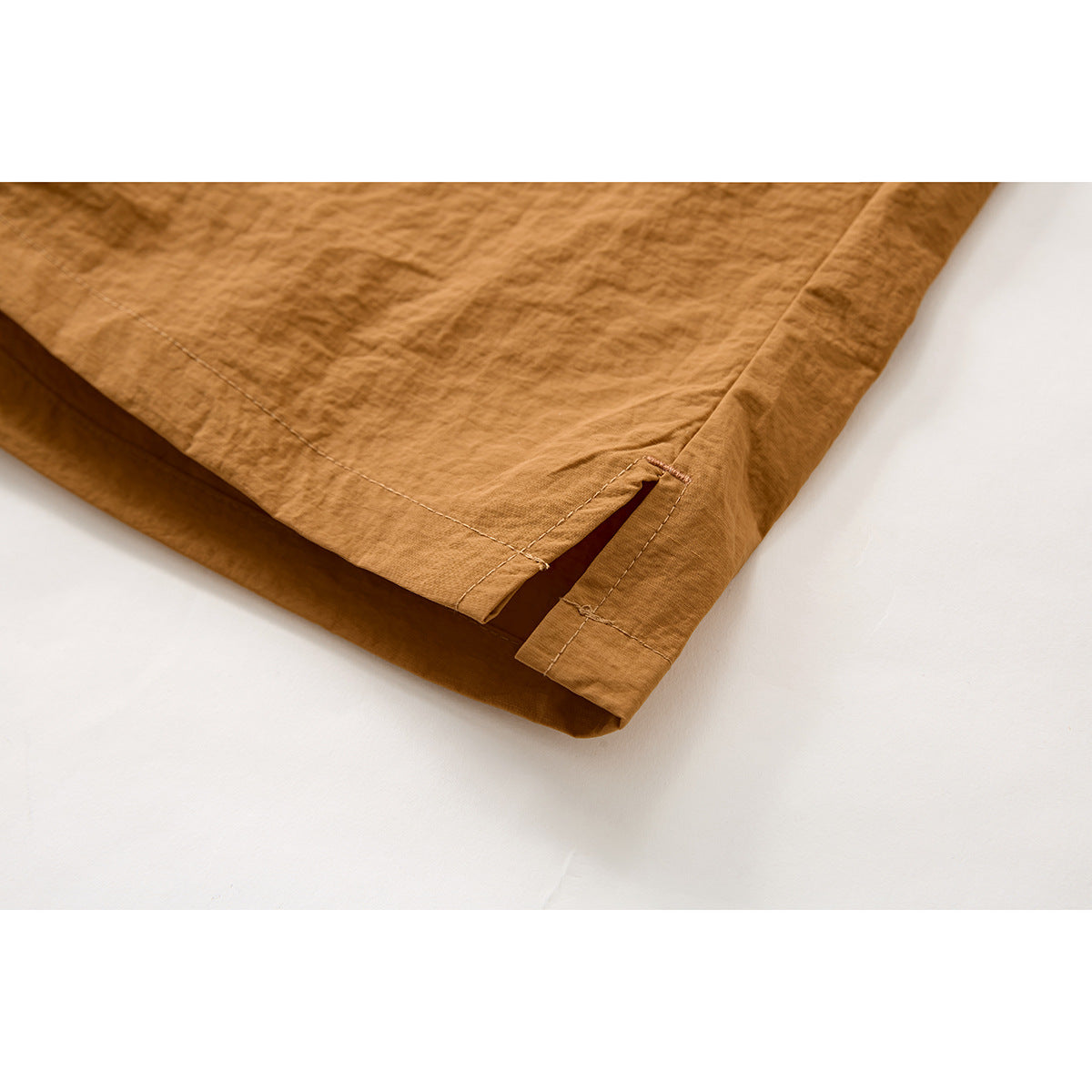 Close-up of the ochre shorts' hem, showing a small side slit and reinforced stitching.